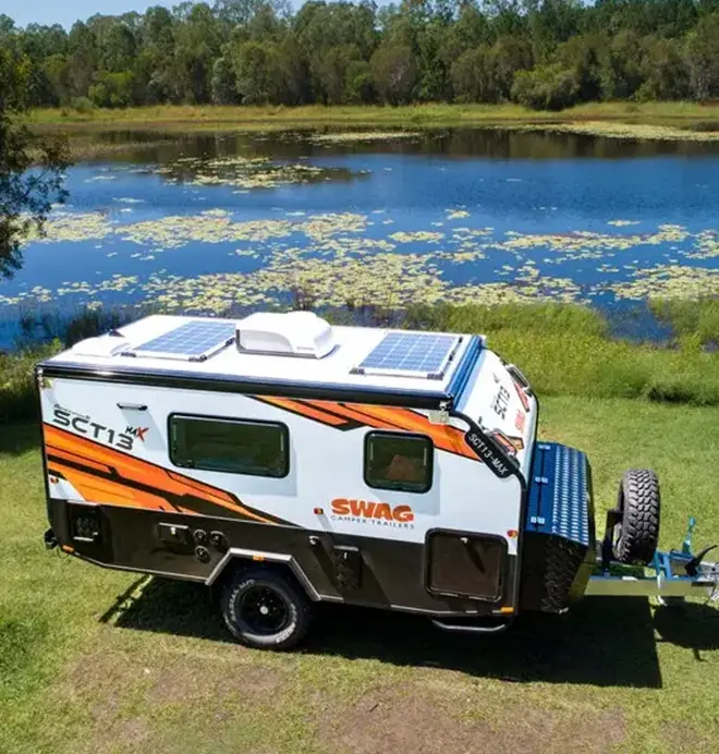 SWAG camper trailer with roof-mounted solar panels beside a lake